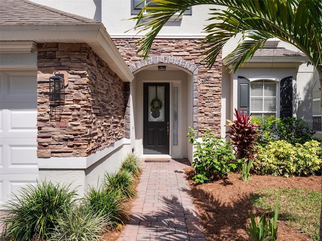 view of exterior entry featuring an attached garage, stone siding, and stucco siding
