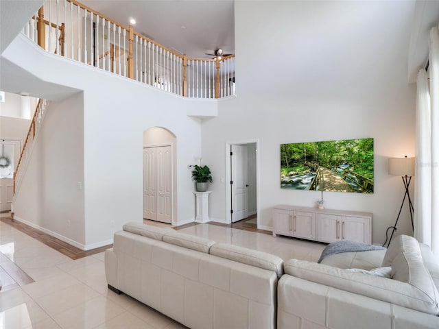 living room with stairs, light tile patterned floors, ceiling fan, baseboards, and a high ceiling