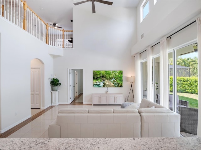 living room with a towering ceiling, tile patterned floors, arched walkways, baseboards, and ceiling fan