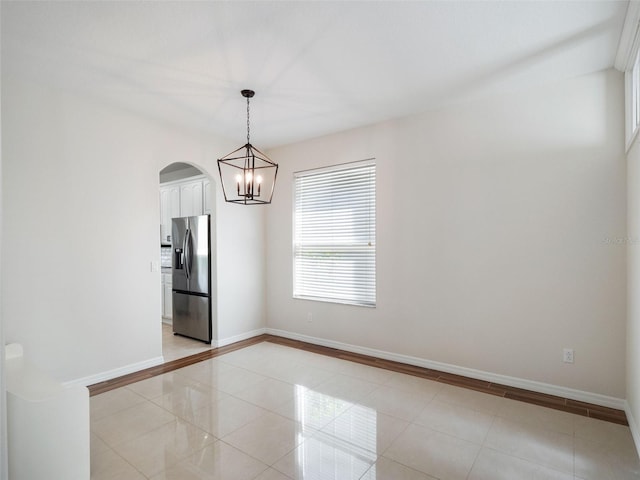 spare room with arched walkways, light tile patterned floors, baseboards, and an inviting chandelier