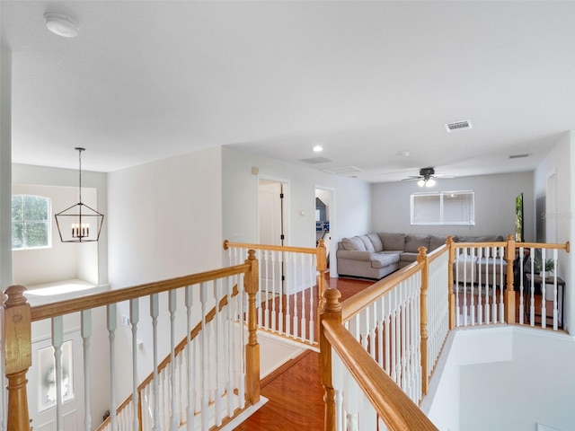 hall with a notable chandelier, wood finished floors, an upstairs landing, and visible vents
