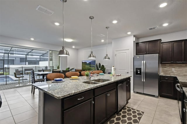 3806 Lana Ave, Davenport, FL 33897 - kitchen featuring appliances with stainless steel finishes, a center island with sink, backsplash, light stone counters, and dark brown cabinetry