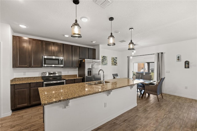 kitchen featuring visible vents, a breakfast bar, a sink, light wood finished floors, and stainless steel appliances