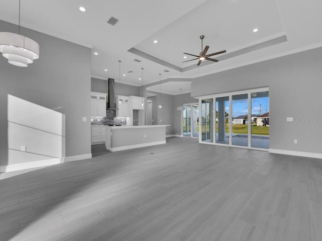 unfurnished living room featuring baseboards, a ceiling fan, a tray ceiling, and visible vents