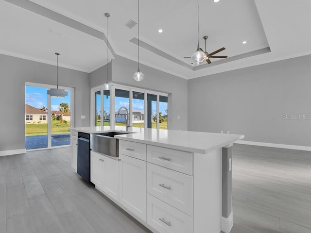 kitchen with a sink, ceiling fan, a tray ceiling, light countertops, and baseboards