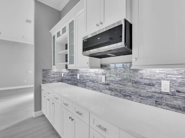 kitchen featuring stainless steel microwave, tasteful backsplash, baseboards, white cabinetry, and glass insert cabinets
