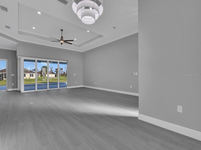 empty room featuring visible vents, a ceiling fan, baseboards, and a raised ceiling