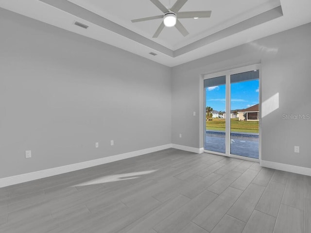 unfurnished room featuring wood finished floors, baseboards, a ceiling fan, and a tray ceiling