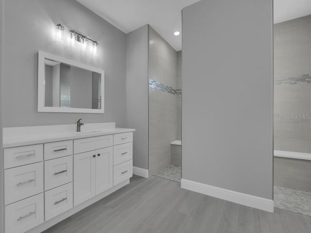 bathroom featuring baseboards, recessed lighting, a walk in shower, wood finished floors, and vanity