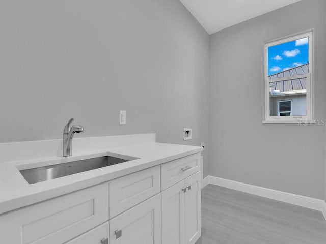 washroom featuring hookup for a washing machine, a sink, cabinet space, light wood finished floors, and baseboards