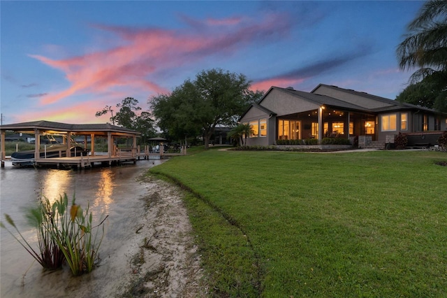 rear view of property featuring driveway, a yard, a water view, and boat lift