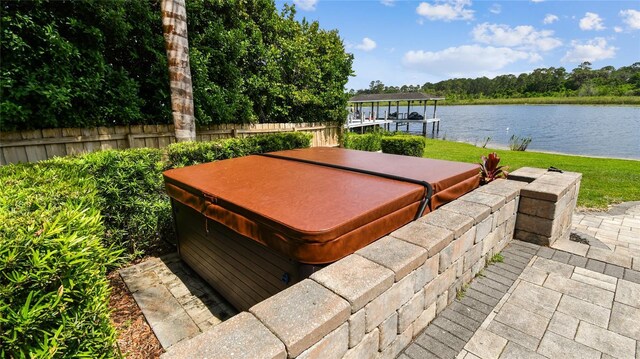 exterior space featuring a water view, a dock, fence, a hot tub, and boat lift