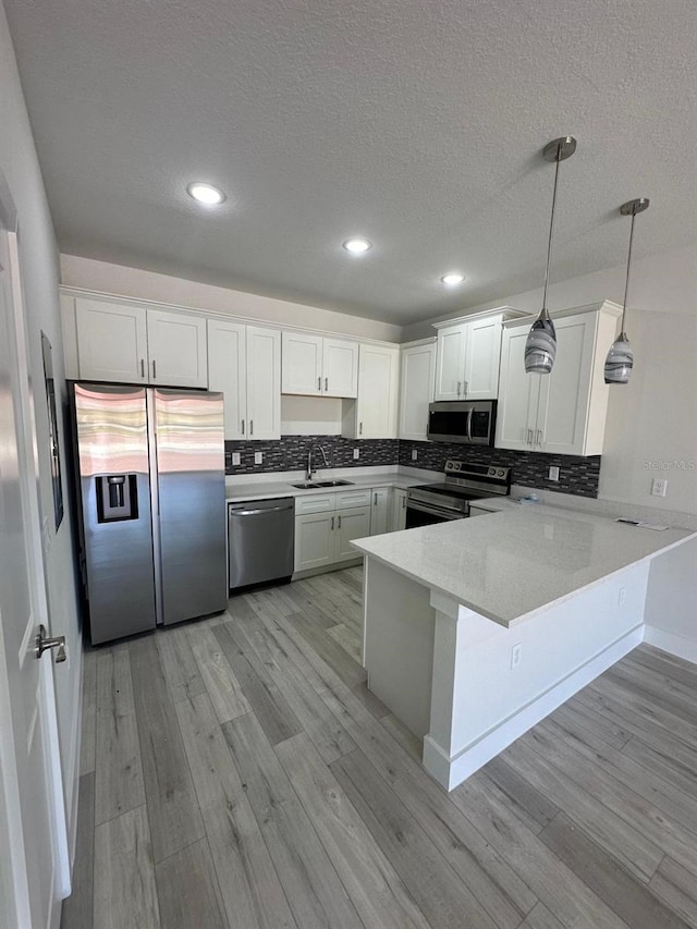kitchen with a peninsula, appliances with stainless steel finishes, a sink, and a textured ceiling