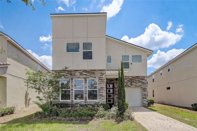 contemporary house with decorative driveway, a garage, stucco siding, and stone siding