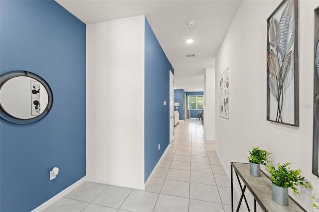 hallway with baseboards, visible vents, and light tile patterned floors