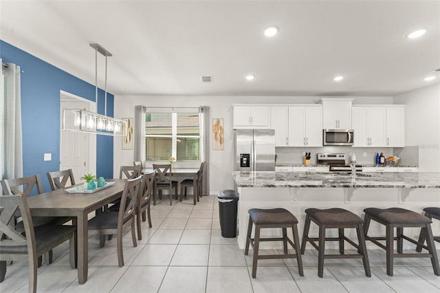 kitchen with pendant lighting, a breakfast bar area, white cabinetry, light stone counters, and appliances with stainless steel finishes