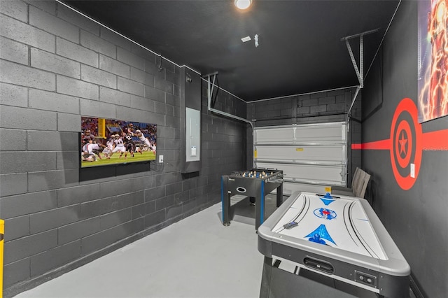 recreation room with a garage, concrete block wall, and concrete flooring
