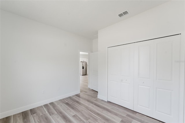 unfurnished bedroom featuring light wood-style flooring, stainless steel fridge with ice dispenser, a closet, baseboards, and visible vents