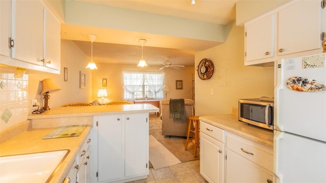 kitchen featuring white cabinets, a peninsula, stainless steel microwave, freestanding refrigerator, and ceiling fan