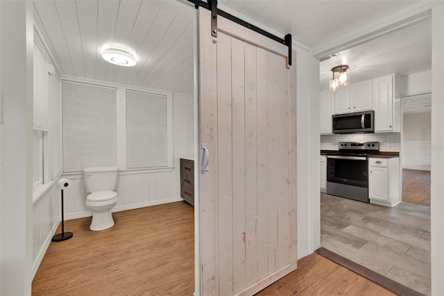 508 10th St, Saint Cloud, FL 34769 - kitchen with stainless steel appliances, a barn door, light wood-style floors, white cabinets, and decorative backsplash