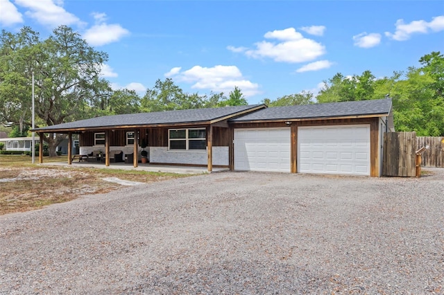ranch-style home with fence, gravel driveway, roof with shingles, and a garage