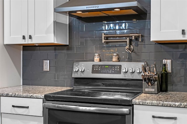 kitchen with decorative backsplash, stainless steel electric stove, white cabinetry, and ventilation hood