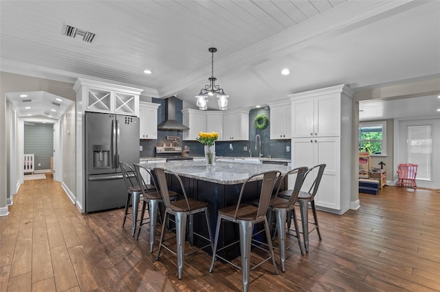 kitchen with visible vents, white cabinetry, wall chimney range hood, a kitchen island, and appliances with stainless steel finishes