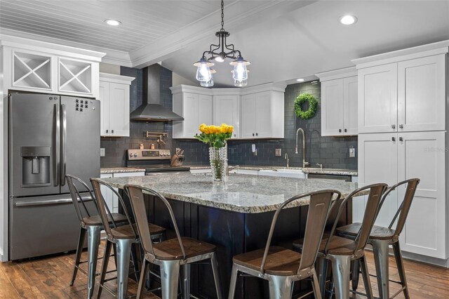 kitchen featuring stainless steel appliances, wall chimney range hood, a sink, dark wood-type flooring, and a center island