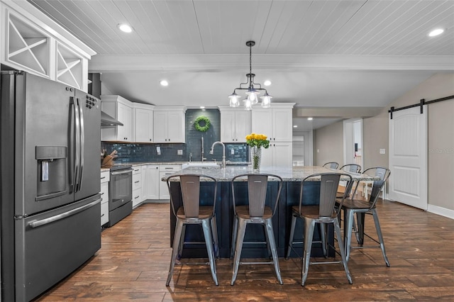 kitchen featuring a barn door, dark wood finished floors, a breakfast bar, wall chimney exhaust hood, and appliances with stainless steel finishes