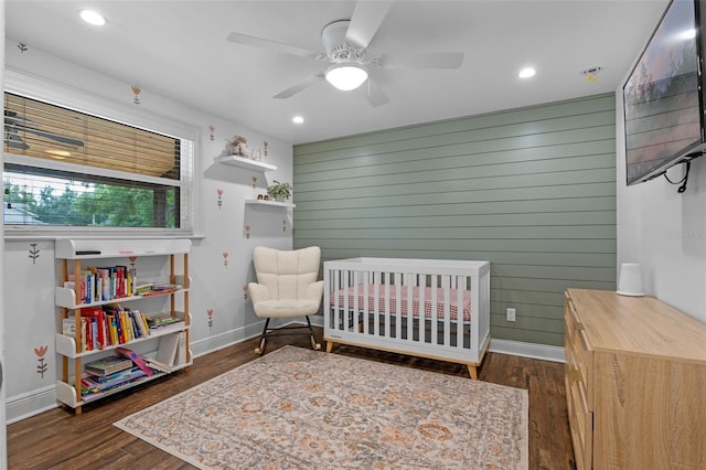 bedroom with a crib, wooden walls, baseboards, dark wood-style floors, and recessed lighting