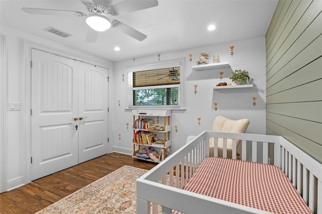 bedroom with a crib, visible vents, a closet, dark wood-style flooring, and ceiling fan