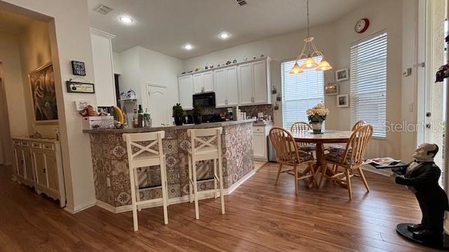 7415 Devereaux St, Reunion, FL 34747 - kitchen featuring black microwave, light wood-type flooring, white cabinets, a breakfast bar area, and recessed lighting