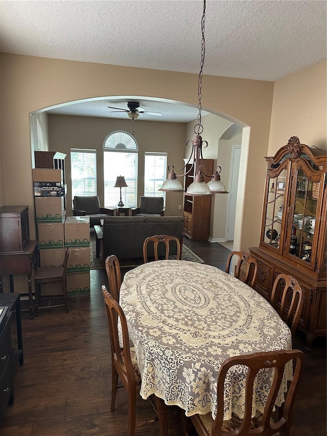dining area featuring arched walkways, a ceiling fan, a textured ceiling, and dark wood-type flooring