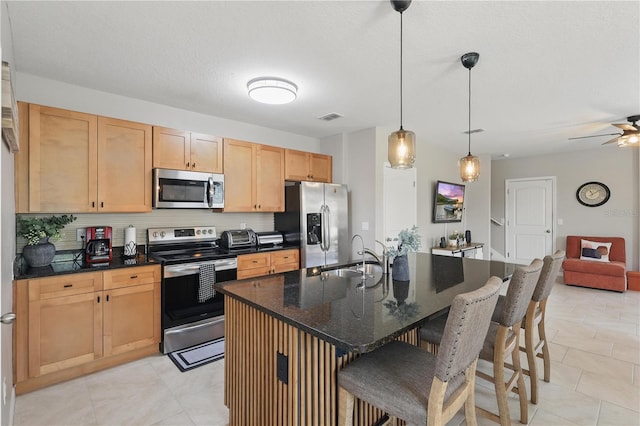 kitchen with appliances with stainless steel finishes, a sink, a breakfast bar, a kitchen island with sink, and a ceiling fan