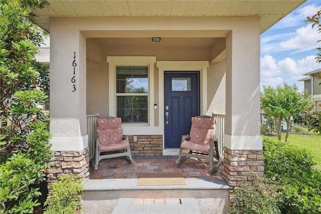 property entrance featuring stucco siding, stone siding, and covered porch