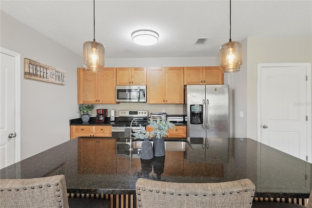 kitchen featuring appliances with stainless steel finishes, decorative light fixtures, a breakfast bar area, and a center island with sink
