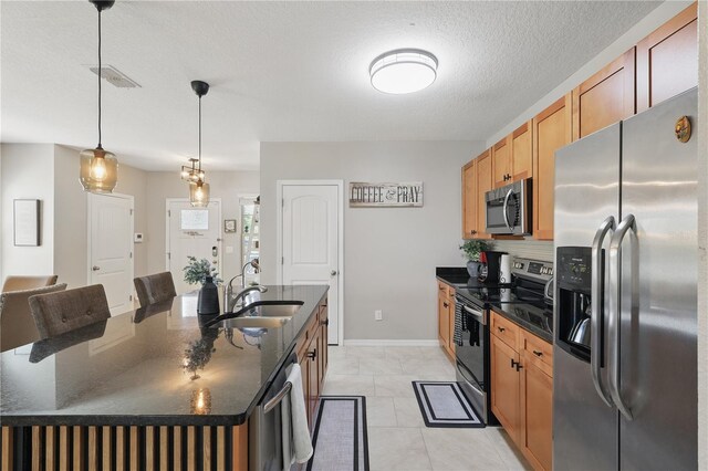 kitchen with appliances with stainless steel finishes, a sink, a kitchen island with sink, tasteful backsplash, and decorative light fixtures