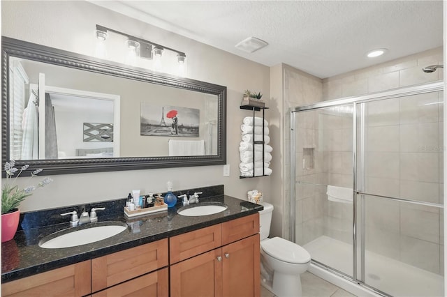 bathroom featuring a shower stall, toilet, a textured ceiling, double vanity, and tile patterned floors