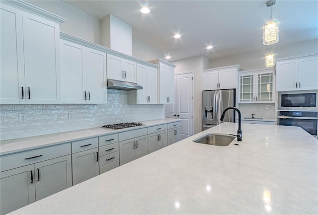 kitchen with a sink, hanging light fixtures, decorative backsplash, appliances with stainless steel finishes, and under cabinet range hood