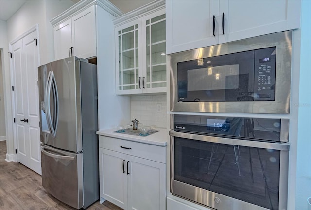 kitchen with light wood finished floors, stainless steel appliances, decorative backsplash, and glass insert cabinets