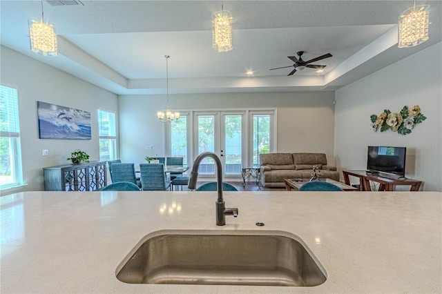 kitchen featuring a sink, open floor plan, pendant lighting, light countertops, and a raised ceiling