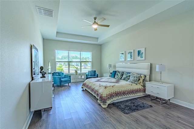 bedroom with a tray ceiling, baseboards, visible vents, wood finished floors, and ceiling fan