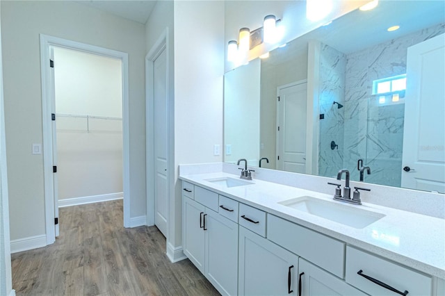 full bathroom featuring wood finished floors, a marble finish shower, a sink, and a walk in closet