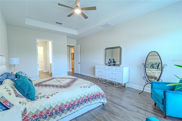 bedroom featuring a raised ceiling, wood finished floors, visible vents, a ceiling fan, and baseboards