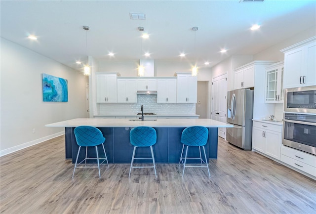 kitchen featuring light wood finished floors, stainless steel appliances, a large island, light countertops, and under cabinet range hood