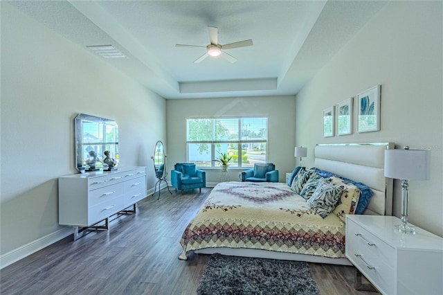 bedroom featuring dark wood-style floors, a tray ceiling, visible vents, a ceiling fan, and baseboards