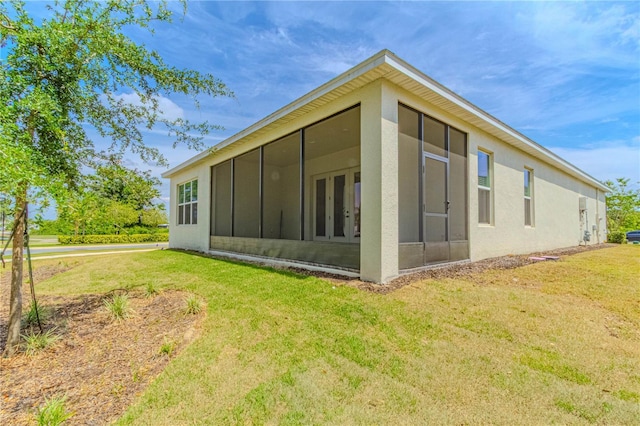 rear view of house featuring stucco siding, a sunroom, french doors, and a lawn