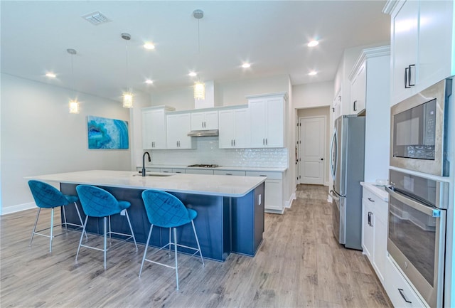 kitchen featuring a sink, light wood-type flooring, light countertops, a breakfast bar, and appliances with stainless steel finishes