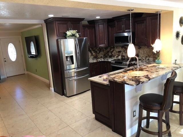 4251 Anthony Ln, Orlando, FL 32822 - kitchen featuring stainless steel appliances, light tile patterned floors, crown molding, a peninsula, and tasteful backsplash