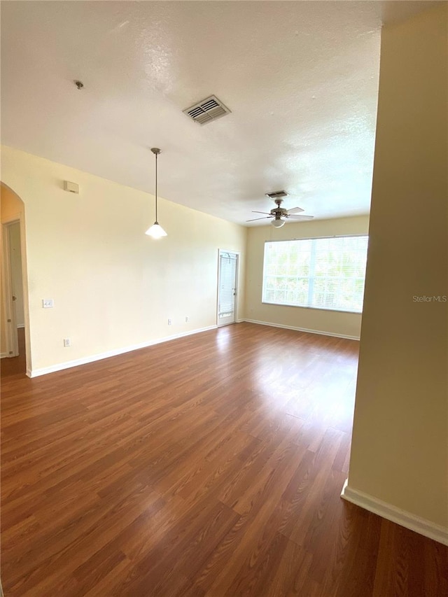 empty room with wood finished floors, ceiling fan, arched walkways, baseboards, and visible vents